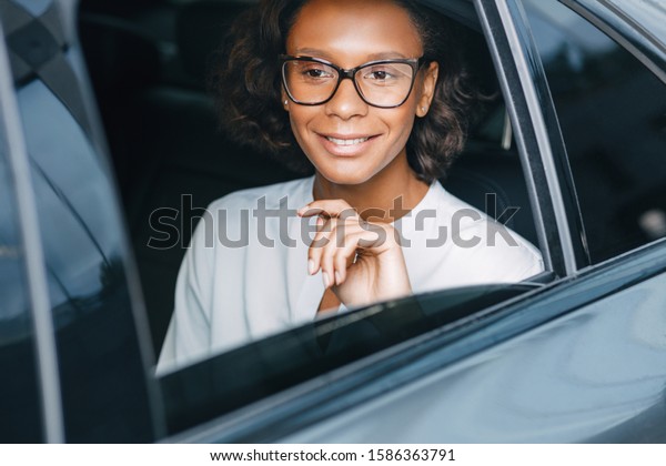 Smiling businesswoman\
sitting on a backseat of the taxi and looking away. Young\
entrepreneur in a car.