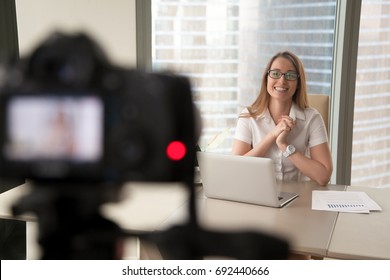 Smiling businesswoman talking on camera, happy entrepreneur vlogger recording business vlog at office desk for videoblog, filming promo ad, making presentation to website, video marketing production - Powered by Shutterstock