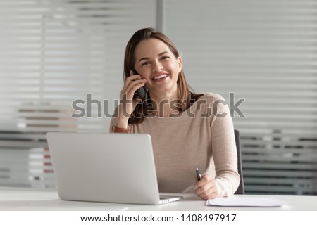 Smiling businesswoman talking on phone make business call at work, happy young entrepreneur female secretary consulting client chatting with friend laughing having mobile conversation in office