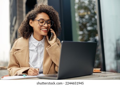 Smiling businesswoman talking phone while working online sitting in cafe terrace - Powered by Shutterstock