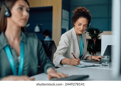 Smiling businesswoman using laptop and taking notes while working in the office.  - Powered by Shutterstock