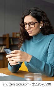 Smiling Businesswoman Using Mobile At Workplace, Young Female Employee Sitting At Office Desk, Looking At Phone Screen And Typing Sms Message With Positive Smile, Distracted From Work, Chatting Online