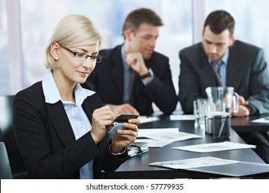 Smiling businesswoman using smartphone at office meeting with colleagues in background.? - Powered by Shutterstock