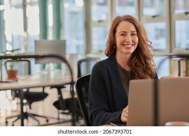 Smiling businesswoman working on a laptop at an office desk - Shutterstock ID 2067393701