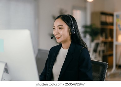 Smiling businesswoman works at her desk, talking on a headset. She embodies professionalism and happiness in the office, engaging in communication and technology