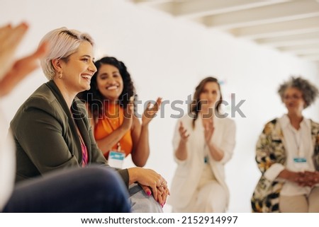 Smiling businesswomen applauding their colleague during a conference meeting in a modern workplace. Group of successful businesswomen working together in an all-female startup.