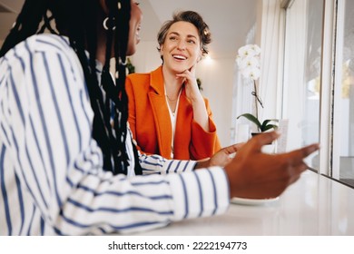 Smiling Businesswomen Having A Discussion While Sitting Together In A Coffee Shop. Two Happy Female Business Colleagues Sharing Ideas During A Coffee Meeting In A Cafe.