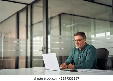 Smiling busy older professional business man working on laptop sitting at desk. Older mature Indian businessman, happy male executive manager typing on computer using pc technology in office. - Powered by Shutterstock