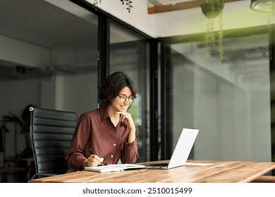 Smiling busy young professional businesswoman hr manager executive looking at laptop computer in office working sitting at desk. Woman employee having online meeting e-learning at work, writing notes. - Powered by Shutterstock