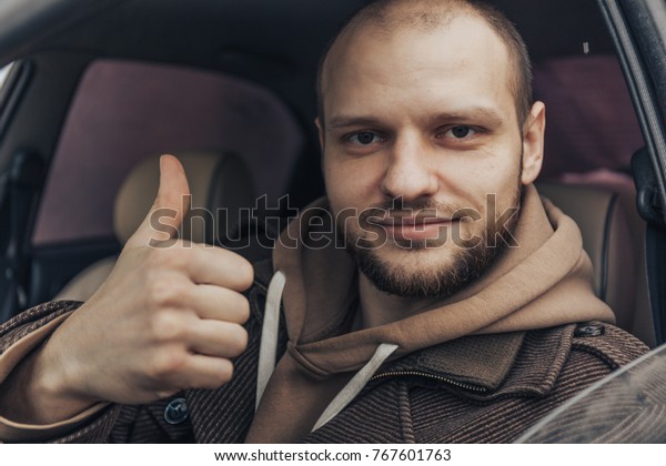 Smiling calm man sitting inside car showing\
thumbs up. Positive driver person,\
toned