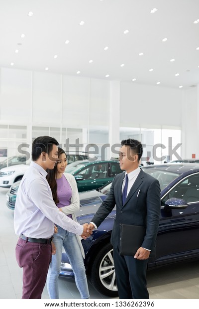 Smiling car dealership manager shaking hand of\
customers before showing\
assortment