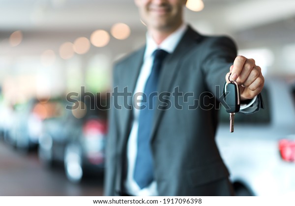Smiling car salesman handing over your new car\
keys, dealership and sales\
concept