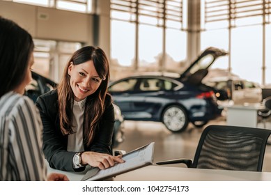 Smiling car saleswoman discussing  a contract with a female customer.
