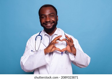 Smiling Cardiology Doctor Making Heart Shape With Hands To Show Care For Health Care And Patients. Happy Medic In Lab Coat With Stethoscope Doing The Hand Gesture For Love.