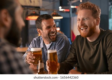 Smiling carefree friends enjoying drinking together in bar. Group of happy young men drinking cold draft beer, chatting and having good time at pub. Laughing men on night out drinking beer on counter. - Powered by Shutterstock