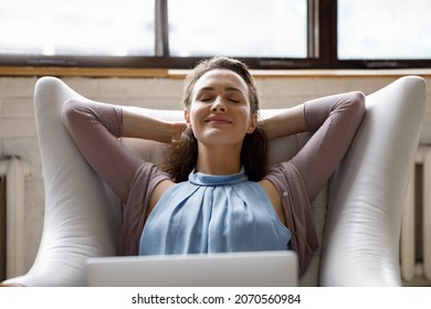 Smiling carefree young beautiful woman breathing fresh air, lying in comfy armchair with folded hands behind head, distracted from computer work daydreaming sleeping, enjoying peaceful moment.