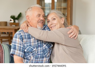 Smiling caring elderly wife embracing senior husband at home. Happy old woman hugging loving mature man. Portrait of retired family married couple dating on weekend.