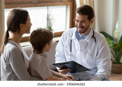 Smiling Caring Male Pediatrician Talk Consult Small Boy Patient At Consultation In Hospital With Mother. Happy Doctor Do Checkup Examine Little Child At Visit To Clinic With Mom. Healthcare Concept.