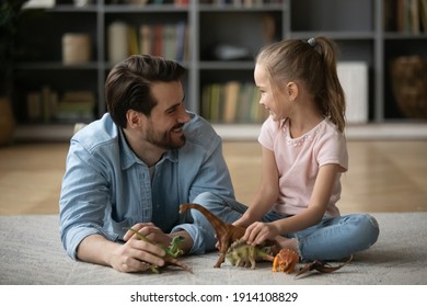 Smiling Caring Young Father Lying On Floor Carpet, Enjoying Playing Toys With Cute Energetic Little 6 Years Old Kid Daughter In Living Room, Happy Two Generations Family Entertaining Together At Home.