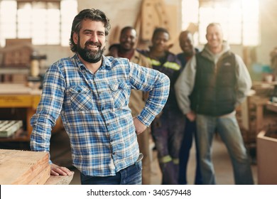 A smiling carpenter with his staff in the background - Shutterstock ID 340579448