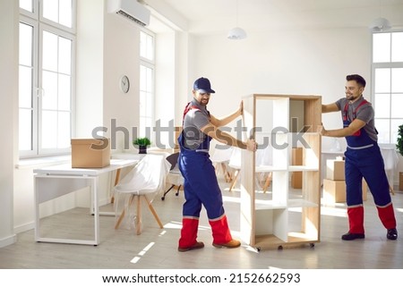 Smiling carriers help customer with furniture during relocation and moving day. Deliverymen or movers in uniform carry shelves work for client at office or new home settle. Transportation concept. Сток-фото © 