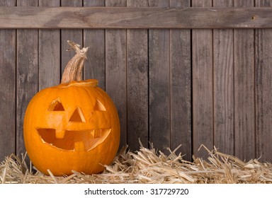 Smiling carved pumpkin on a straw surface against a rustic wood background with copy space