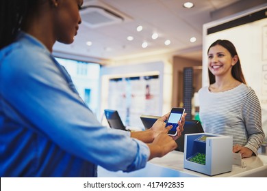 Smiling Cashier In Striped Blouse Watching Customer Pay At Register With Phone In Eyeglasses Store