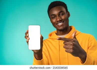 Smiling casual black man pointing at blank white cell phone screen in studio - Shutterstock ID 2143334565