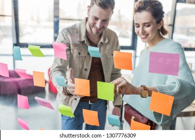 smiling casual businessman and businesswoman putting colorful sticky notes on glass window in office - Powered by Shutterstock