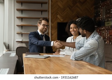 Smiling Caucasian businessman realtor and African American family, tenants shaking hands at meeting, making successful investment or insurance deal, happy couple purchasing real estate, handshaking