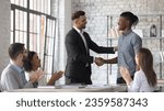 Smiling Caucasian businessman shake hand congratulate with good work achievement result african American male employee, boss handshake greeting with promotion excited biracial worker at meeting