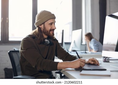 Smiling caucasian businessman writing in graphics tablet and watching on computer during work at office. Concept of business and entrepreneur lifestyle. Blur of female colleague of man on background - Powered by Shutterstock