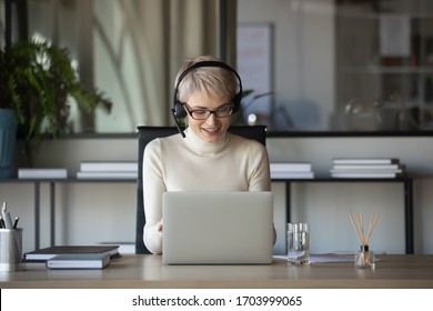 Smiling Caucasian Businesswoman Sit At Desk In Office Talk On Webcam With Business Client Wearing Headset, Middle-aged Woman In Headphones Have Video Call Consult Customer Online On Laptop