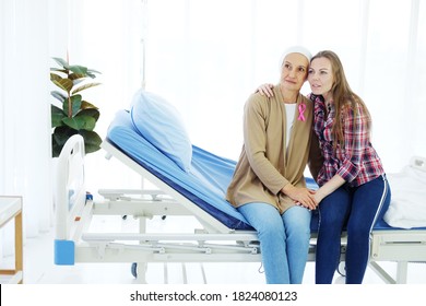 Smiling Caucasian Elderly Mother in white headscarf is sitting with young daughter on bed together in hospital after chemotherapy because she is suffering from cancer or Leukemia patient.