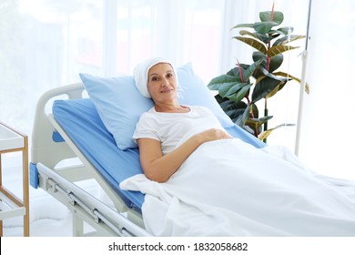 Smiling Caucasian Elderly Mother In White Headscarf Is Laying On Bed In Hospital After Chemotherapy Because She Is Suffering From Cancer Or Leukemia Patient.