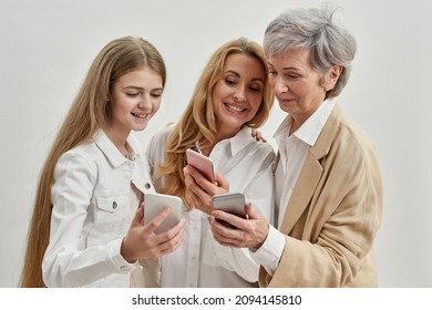 Smiling caucasian family of three female generations using and watching smartphones of each other. Age and generation concept. Grandmother, mother and granddaughter. White background. Studio shoot - Powered by Shutterstock