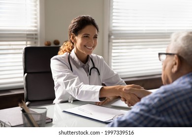 Smiling Caucasian Female Doctor In White Medical Uniform Shake Hand Of Old Male Patient In Hospital. Happy Woman GP Handshake Senior Man Close Health Insurance Deal In Clinic. Healthcare Concept.