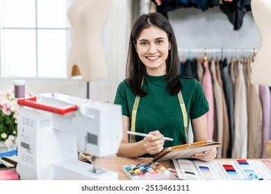 Smiling caucasian female fashion designer works in studio by idea drawing sketches with digital tablet and colorful fabric for a dress design collection, choose clothing colors for tailoring - Powered by Shutterstock