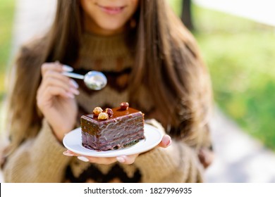 Smiling Caucasian Female Model Eating Fancy Slice Cake In Outdoor On Background Of Green Park, Enjoying Gentle Chocolate Dessert And Coffee , Girl Eat Sweet Cake