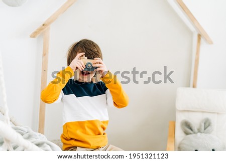 Smiling caucasian little Cute preschooler child boy having fun and playing. Kid acting like a professional photographer taking photos at home in kids room. Background with copy space