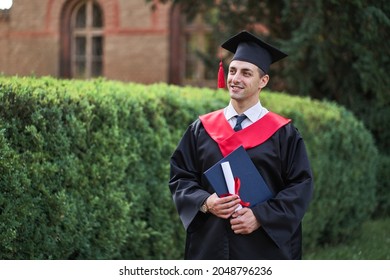 Smiling Caucasian Male Graduate Student In Graduation Robe With Iploma.