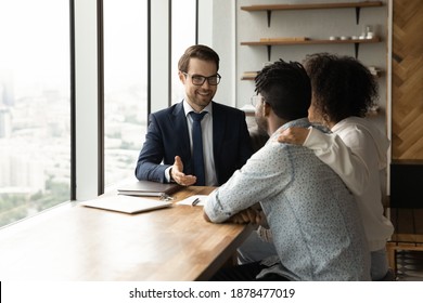 Smiling Caucasian male realtor talk with biracial couple at meeting, consult about house purchase or rent. Real estate agent have consultation with African American family clients about home rental.