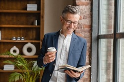Smiling Caucasian Mature Middle-aged Businessman Ceo Boss Lawyer Freelancer Drinking Coffee Hot Beverage Reading Book Working At Office Looking At The Window