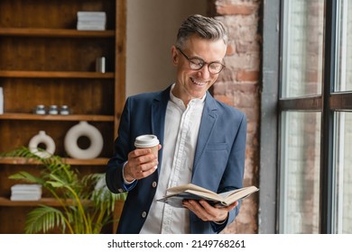 Smiling caucasian mature middle-aged businessman ceo boss lawyer freelancer drinking coffee hot beverage reading book working at office looking at the window - Powered by Shutterstock