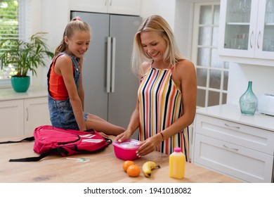 Smiling Caucasian Mother Preparing Daughter Packed Lunch In Kitchen. Happy Family Spending Time Together At Home.