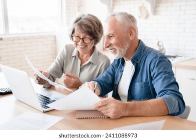 Smiling caucasian old elderly senior couple husband and wife using laptop and doing paperwork together at home kitchen. E-banking, e-commerce - Powered by Shutterstock