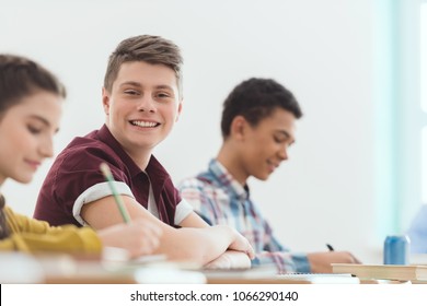 Smiling caucasian schoolboy sitting at desk between classmates - Powered by Shutterstock