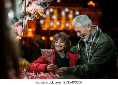 A smiling Caucasian senior treats his joyful grandson to hard candy in a festive market environment, surrounded by colorful confections and seasonal decor. - Powered by Shutterstock