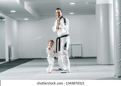 Smiling Caucasian Taekwondo Trainer Posing With Little Girl In White Gym.