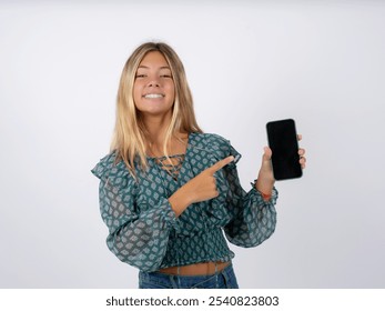 Smiling caucasian teen girl wearing green dress over white  Mock up copy space. Pointing index finger on mobile phone with blank empty screen - Powered by Shutterstock